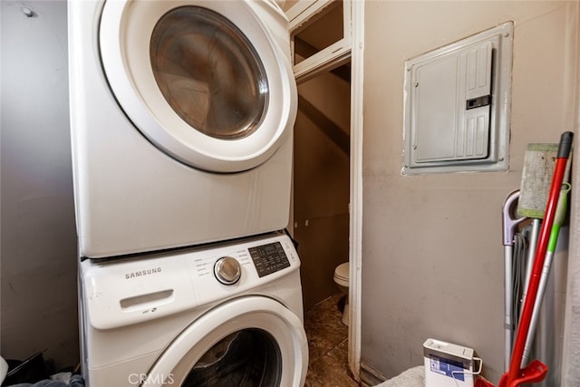 washroom with dark tile patterned flooring, stacked washer / dryer, and electric panel