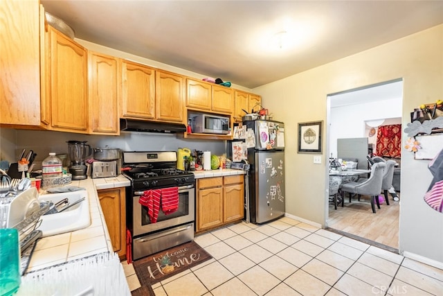 kitchen featuring appliances with stainless steel finishes, light wood-type flooring, sink, and tile countertops