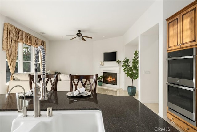 kitchen with ceiling fan, dark stone counters, and stainless steel double oven