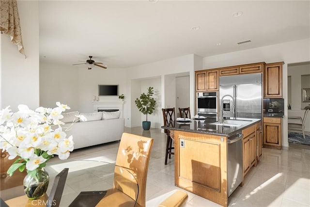 kitchen featuring ceiling fan, a kitchen bar, an island with sink, stainless steel appliances, and light tile patterned floors