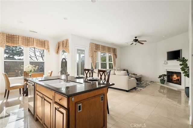 kitchen with dark stone countertops, sink, a kitchen island with sink, ceiling fan, and stainless steel dishwasher