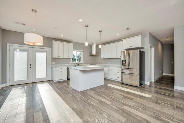 kitchen with appliances with stainless steel finishes, a center island, white cabinetry, wall chimney range hood, and hanging light fixtures