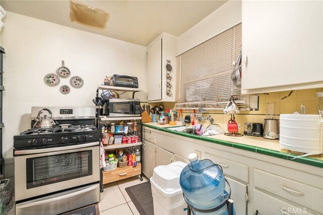 kitchen featuring tile counters, light tile patterned flooring, white cabinetry, decorative backsplash, and stainless steel appliances