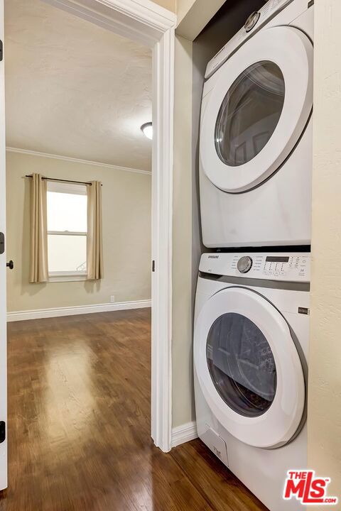 laundry area featuring stacked washer / dryer, crown molding, and dark hardwood / wood-style flooring