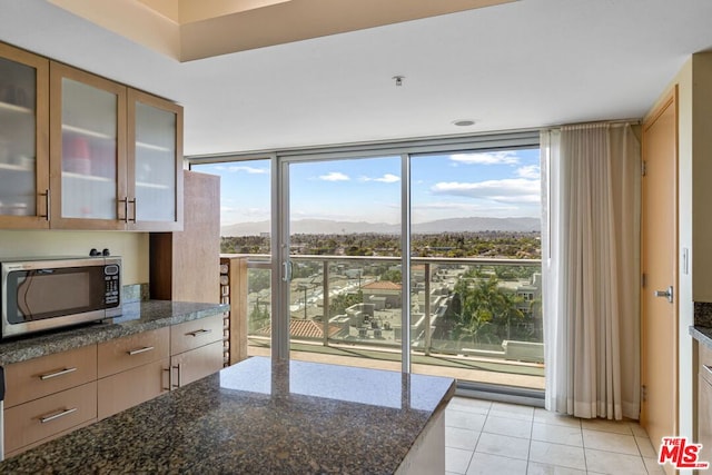 kitchen with a mountain view, a healthy amount of sunlight, dark stone counters, and light tile patterned flooring