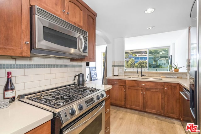 kitchen with appliances with stainless steel finishes, sink, backsplash, and light hardwood / wood-style floors