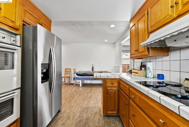 kitchen featuring backsplash, tile countertops, stainless steel fridge, light hardwood / wood-style floors, and a textured ceiling