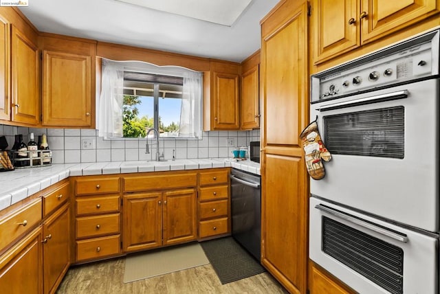 kitchen featuring tasteful backsplash, stainless steel dishwasher, sink, light hardwood / wood-style flooring, and tile counters