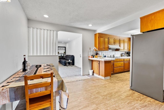 kitchen featuring stainless steel fridge, a textured ceiling, black electric cooktop, tile countertops, and light hardwood / wood-style flooring