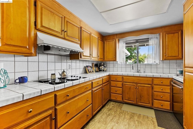 kitchen with tile counters, light wood-type flooring, sink, and tasteful backsplash