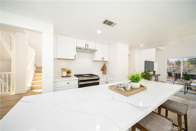 kitchen featuring stainless steel gas range oven, light hardwood / wood-style flooring, light stone countertops, tasteful backsplash, and white cabinetry