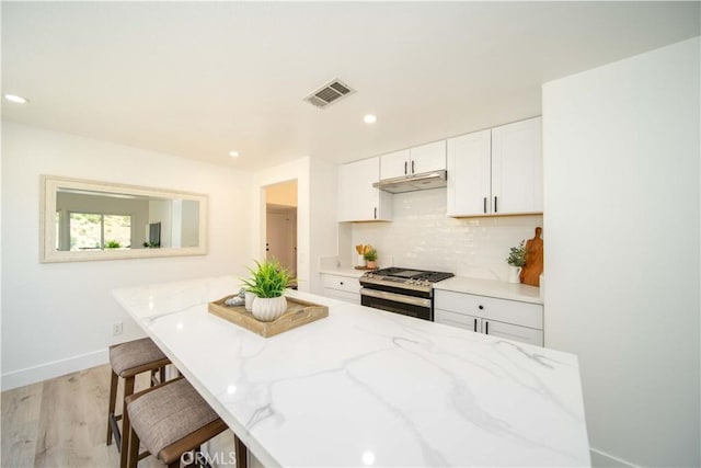 kitchen featuring light stone counters, a breakfast bar, light hardwood / wood-style floors, white cabinetry, and stainless steel range with gas stovetop