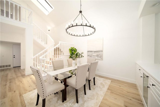 dining space with a notable chandelier, a skylight, high vaulted ceiling, and light hardwood / wood-style flooring