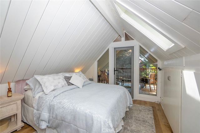 bedroom with vaulted ceiling with skylight, light hardwood / wood-style flooring, and access to outside