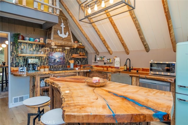 kitchen featuring refrigerator, black gas cooktop, lofted ceiling with beams, sink, and light wood-type flooring