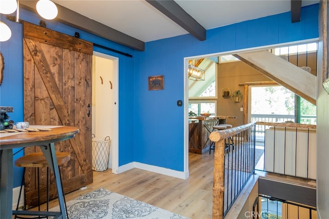 interior space featuring wood walls, a barn door, beam ceiling, and light wood-type flooring