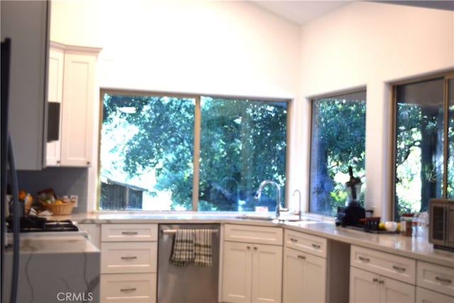 kitchen with stainless steel dishwasher, sink, white cabinets, and light stone countertops