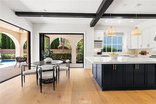 kitchen with decorative backsplash, light wood-type flooring, pendant lighting, beamed ceiling, and white cabinets