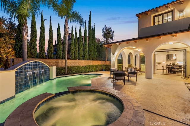 pool at dusk with an in ground hot tub, an outdoor living space, pool water feature, and a patio area