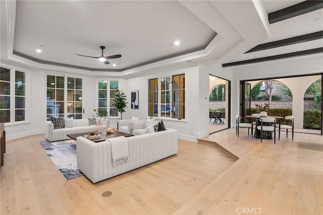 living room featuring light hardwood / wood-style floors, plenty of natural light, a tray ceiling, and ceiling fan