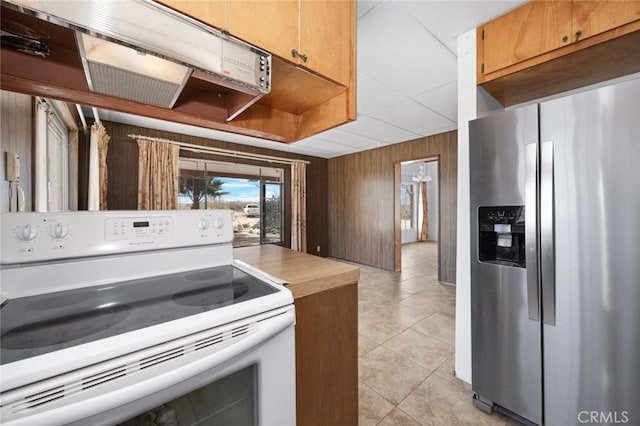 kitchen featuring stainless steel refrigerator with ice dispenser, wooden walls, light tile patterned floors, and white range with electric stovetop