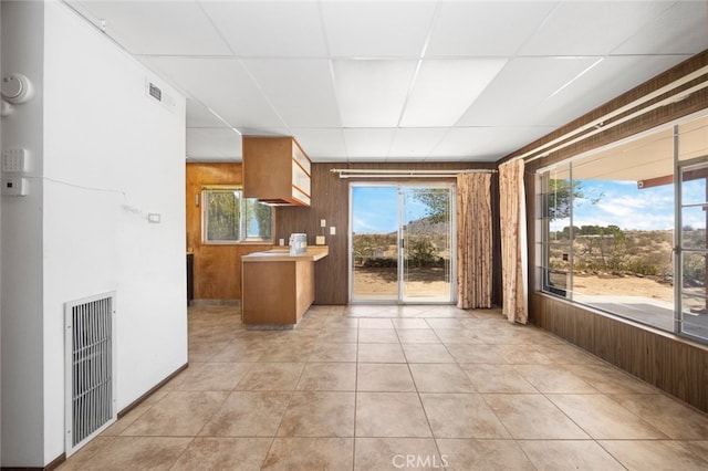 kitchen featuring a drop ceiling, wooden walls, light tile patterned floors, and a healthy amount of sunlight