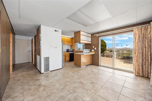 kitchen with kitchen peninsula, wooden walls, a drop ceiling, and light tile patterned flooring