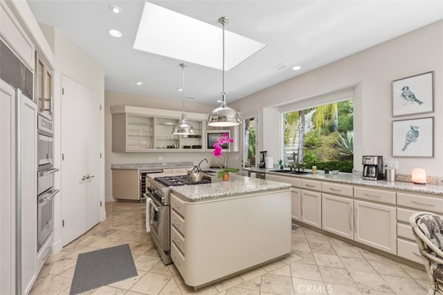 kitchen with pendant lighting, a center island with sink, stainless steel stove, a skylight, and light stone counters