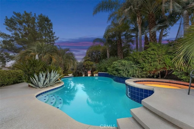 pool at dusk with an in ground hot tub