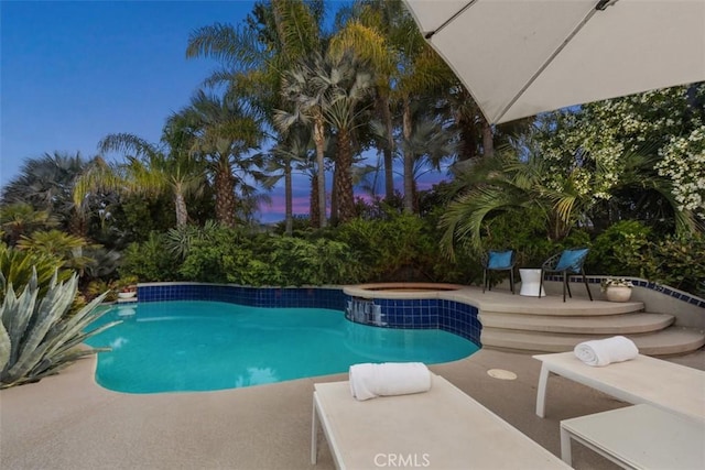 pool at dusk with an in ground hot tub and a patio area