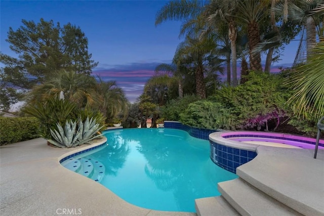 pool at dusk with an in ground hot tub