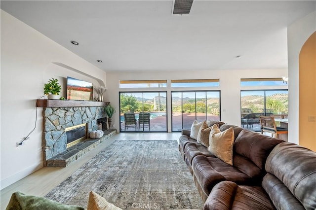 living area featuring a stone fireplace, wood finished floors, visible vents, and baseboards