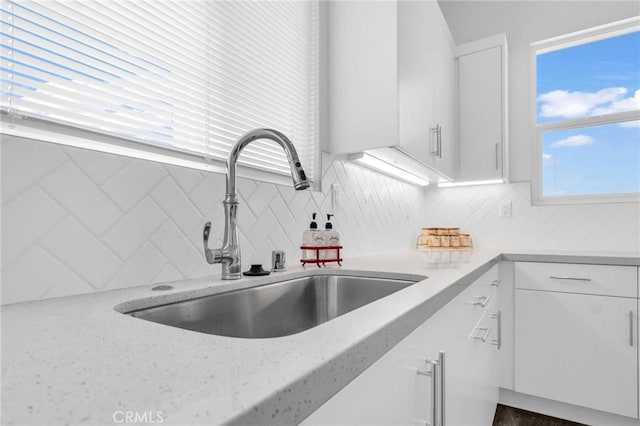 kitchen with backsplash, light stone countertops, white cabinetry, and sink