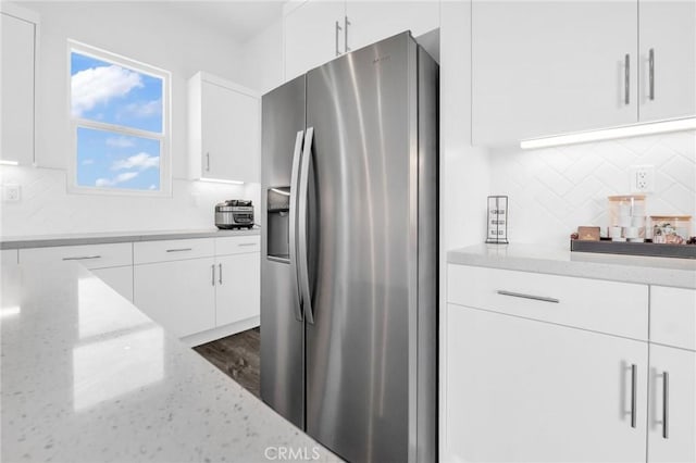 kitchen with decorative backsplash, stainless steel fridge, light stone countertops, white cabinets, and dark hardwood / wood-style floors