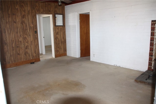 carpeted spare room with wooden walls, ceiling fan, and brick wall