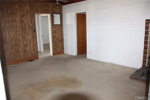 empty room featuring concrete floors, ceiling fan, and wooden walls