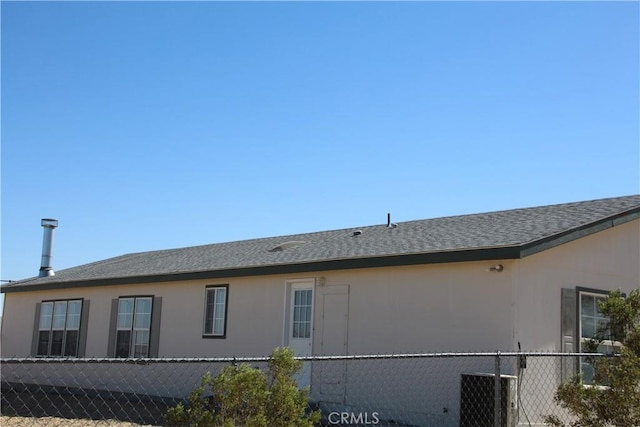 view of side of home featuring cooling unit, roof with shingles, fence, and stucco siding