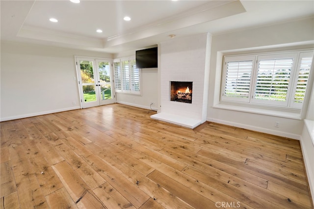 unfurnished living room featuring light hardwood / wood-style flooring, a tray ceiling, and a brick fireplace