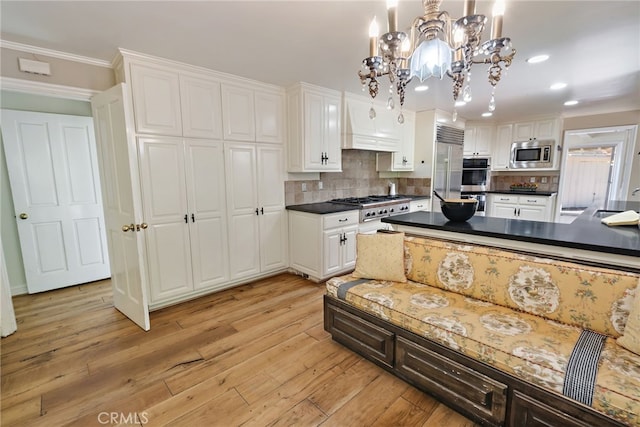 kitchen featuring white cabinets, hanging light fixtures, backsplash, light hardwood / wood-style flooring, and built in appliances