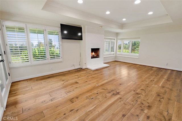 unfurnished living room with light hardwood / wood-style flooring, a wealth of natural light, a tray ceiling, and a brick fireplace