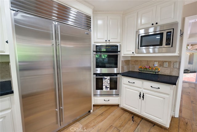 kitchen with built in appliances, tasteful backsplash, white cabinetry, and light hardwood / wood-style floors