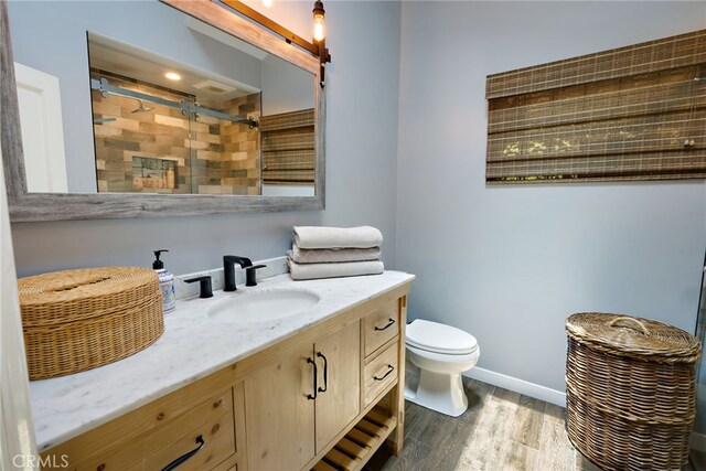 bathroom featuring toilet, hardwood / wood-style flooring, vanity, and tiled shower