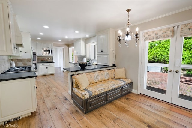 kitchen featuring tasteful backsplash, appliances with stainless steel finishes, light wood-type flooring, hanging light fixtures, and white cabinetry