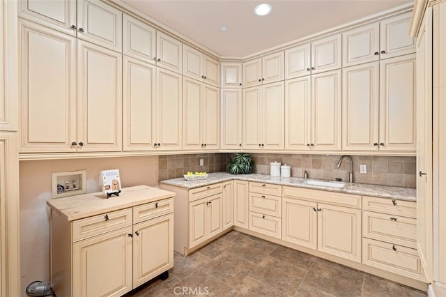 interior space with light stone countertops, cream cabinetry, sink, and tasteful backsplash