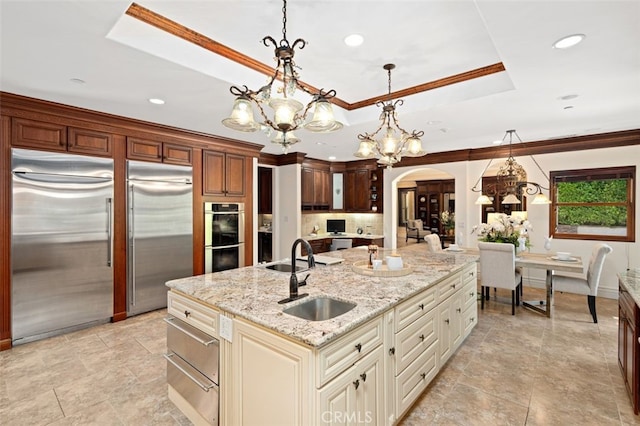 kitchen featuring light stone counters, sink, cream cabinetry, stainless steel appliances, and decorative light fixtures