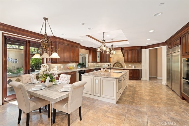 kitchen featuring hanging light fixtures, light stone counters, tasteful backsplash, a kitchen island with sink, and a chandelier