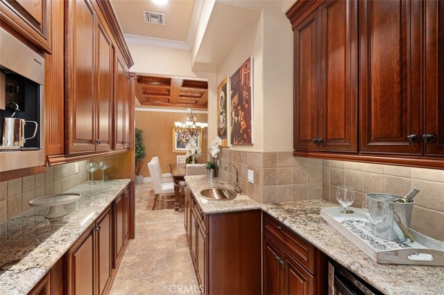 kitchen with hanging light fixtures, sink, a notable chandelier, light stone countertops, and decorative backsplash