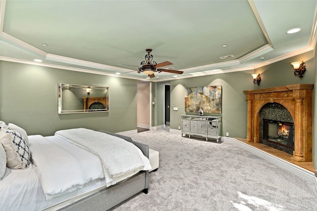 carpeted bedroom with ornamental molding, a tray ceiling, ceiling fan, and a premium fireplace