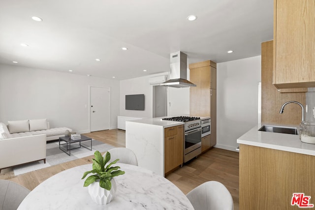 kitchen featuring light brown cabinets, wall chimney exhaust hood, high end range, sink, and light wood-type flooring