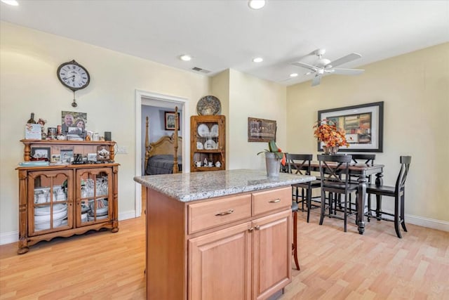 kitchen with ceiling fan, light wood-type flooring, light stone counters, and a kitchen island